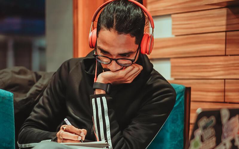 Young man listening and making notes, with orange, over-ear headphones